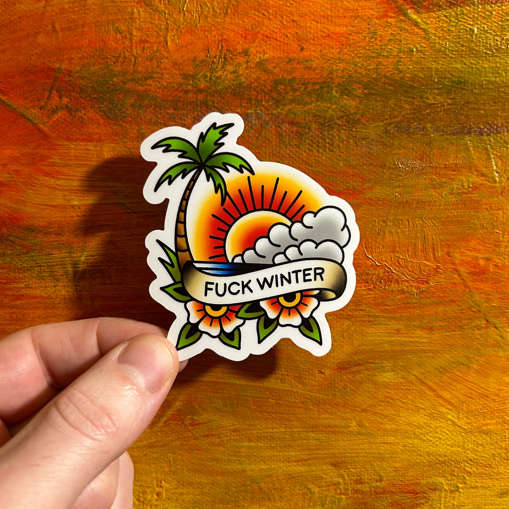 Beautifully coloured illustration of a beach sunset theme with the ocean, a palm tree, sun, clouds and flowers below the banner saying “fuck winter”. A die cut sticker in tattoo style.