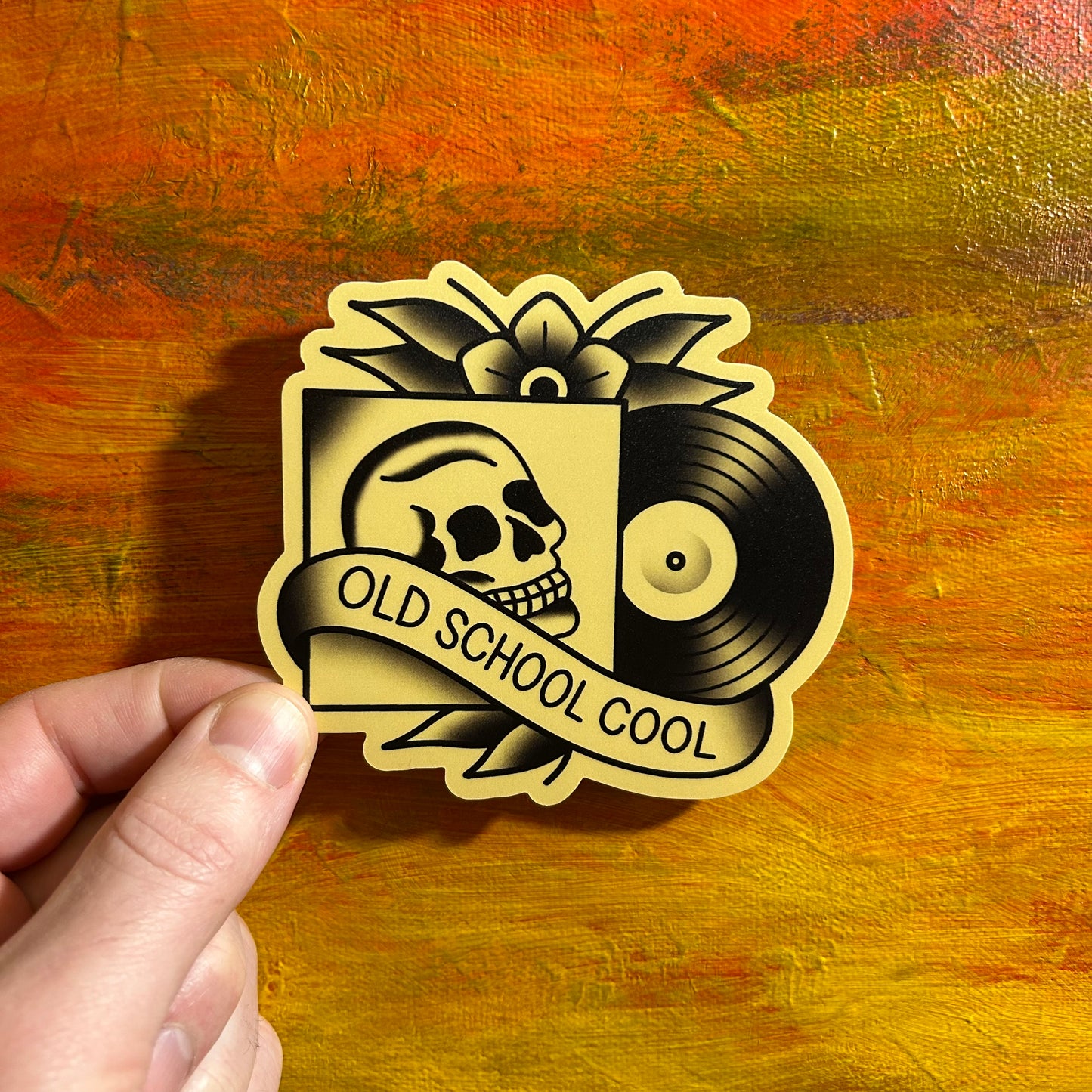 Off white tattoo style sticker of a record and a record sleeve with a skull in it, surrounded with flowers. A banner streaming across the record sleeve says “old school cool”.