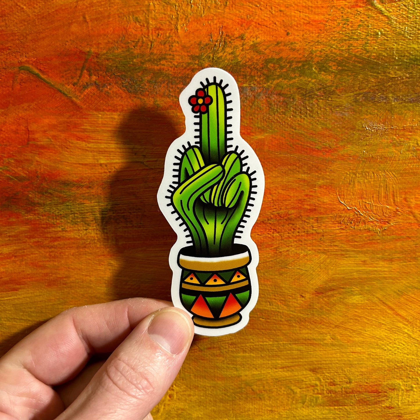 An illustrative sticker of a cactus giving the middle finger. The cactus is bright green with other shades of vibrant green. The pot the cactus is standing in has a western vibe and earthy tones.