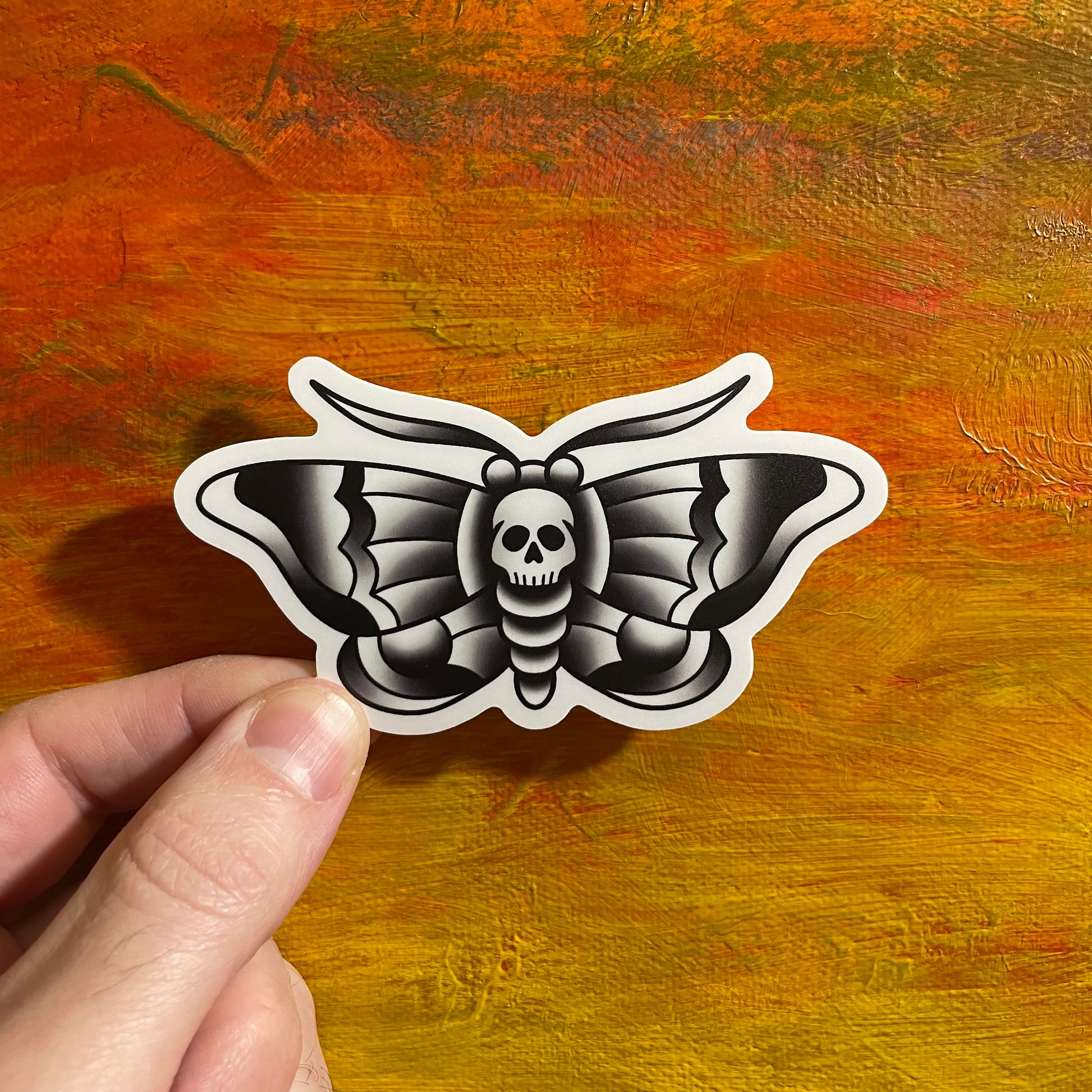 A die cut sticker of a black and white death moth, done in a tattoo style.