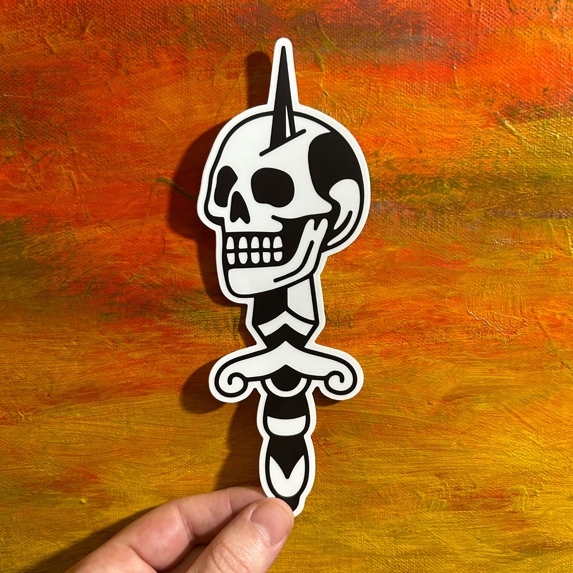 A tall sticker of an illustrative black and white skull stabbed by a sword through the head. Tattoo style, low brow art