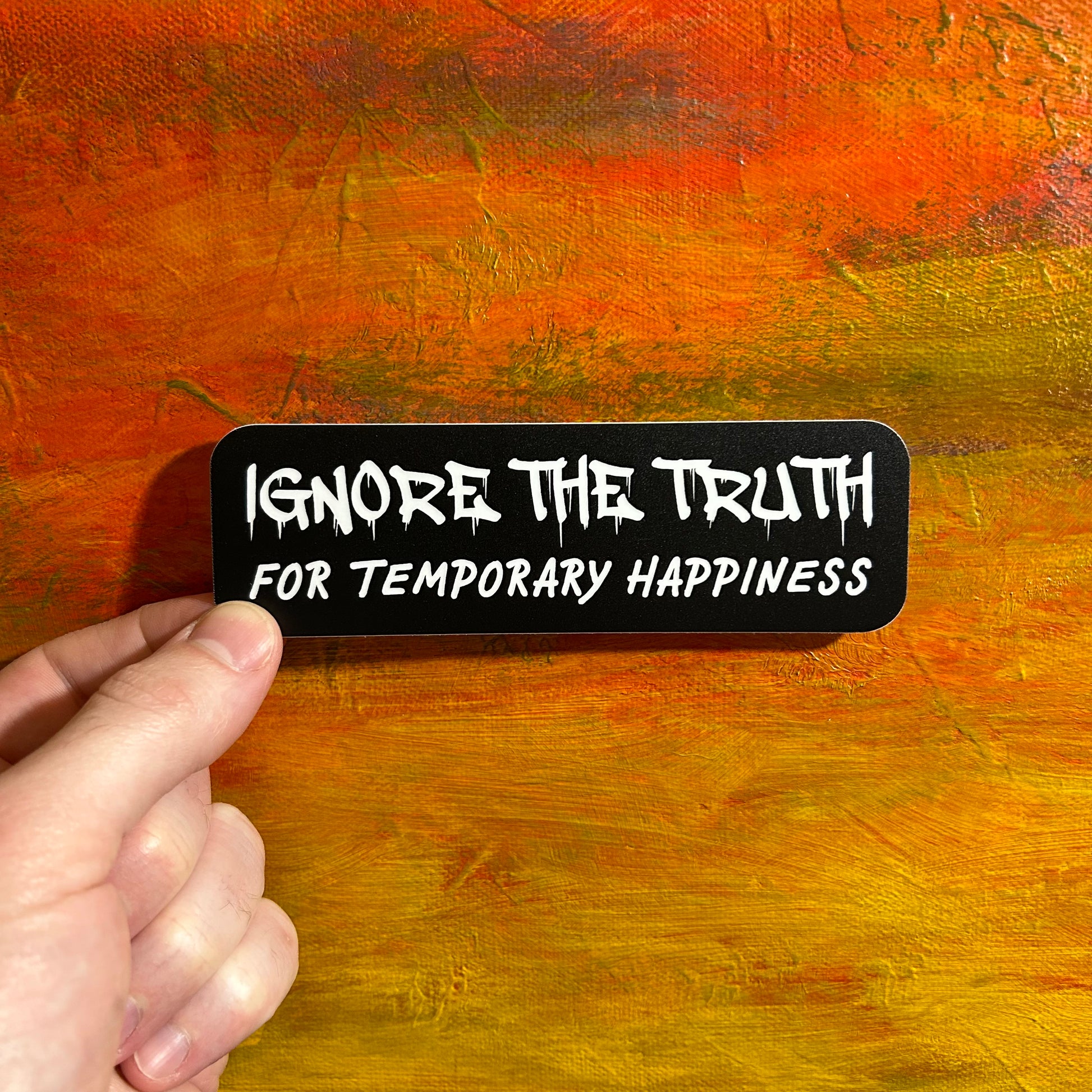 Black rectangular sticker with white graffiti font reading “IGNORE THE TRUTH” and in sign lettering below it says “FOR TEMPORARY HAPPINESS”.