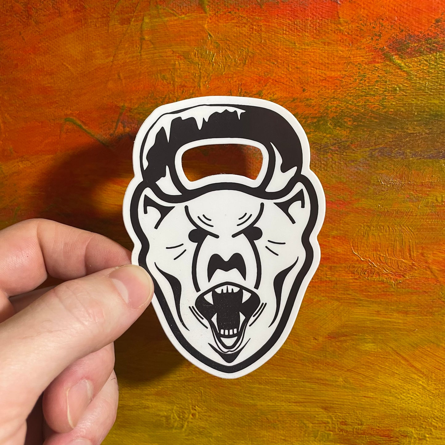 A die cut sticker of a bold contrasting illustration of a polar bear head. Coming out from the top of its head is a kettlebell handle, implying that the kettlebell is the polar bear head