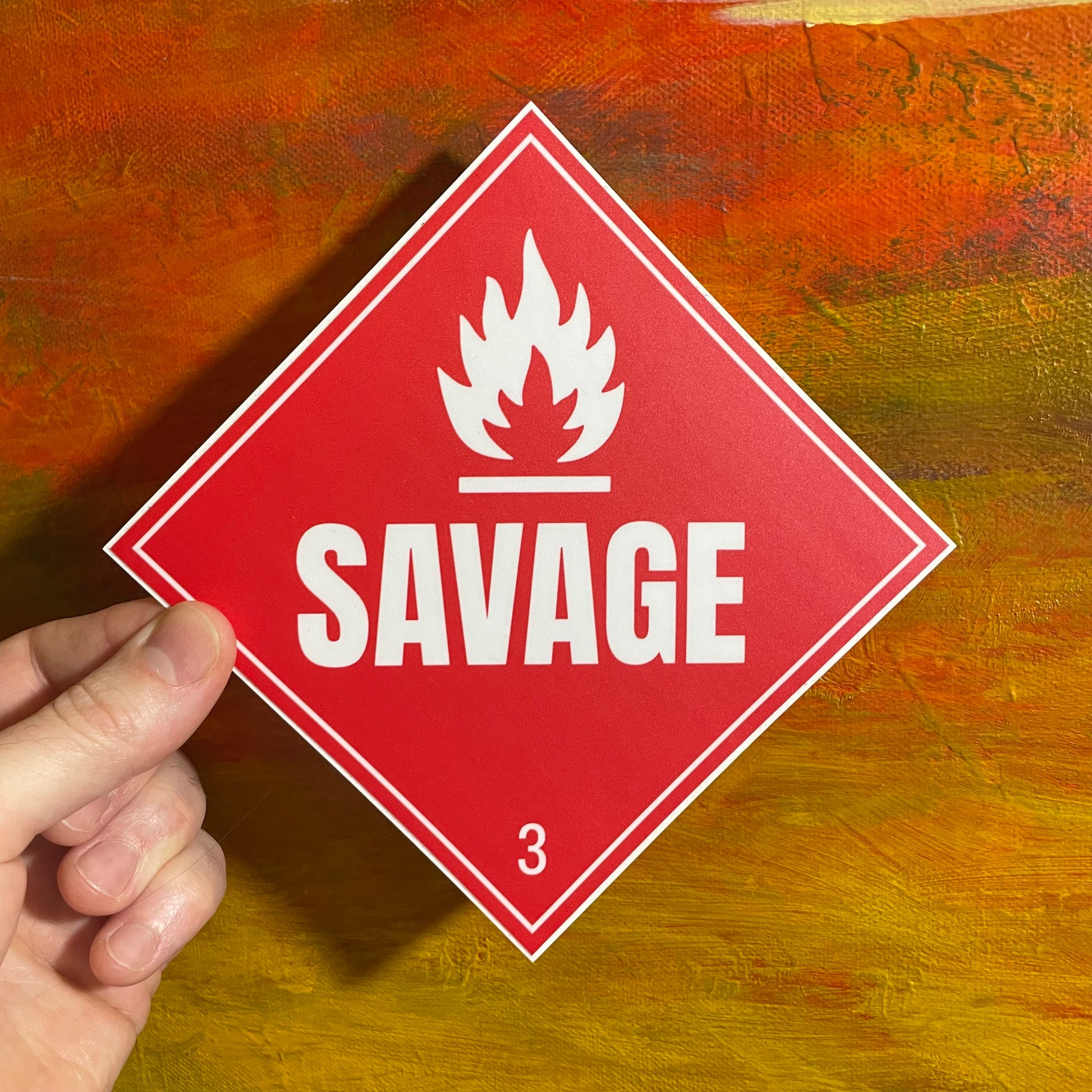 Red square sticker of a fire caution label sticker. There is a white fire symbol and underneath in big bold letters saying “SAVAGE”. A small number 3 sits at the bottom of the square, referencing its danger class.