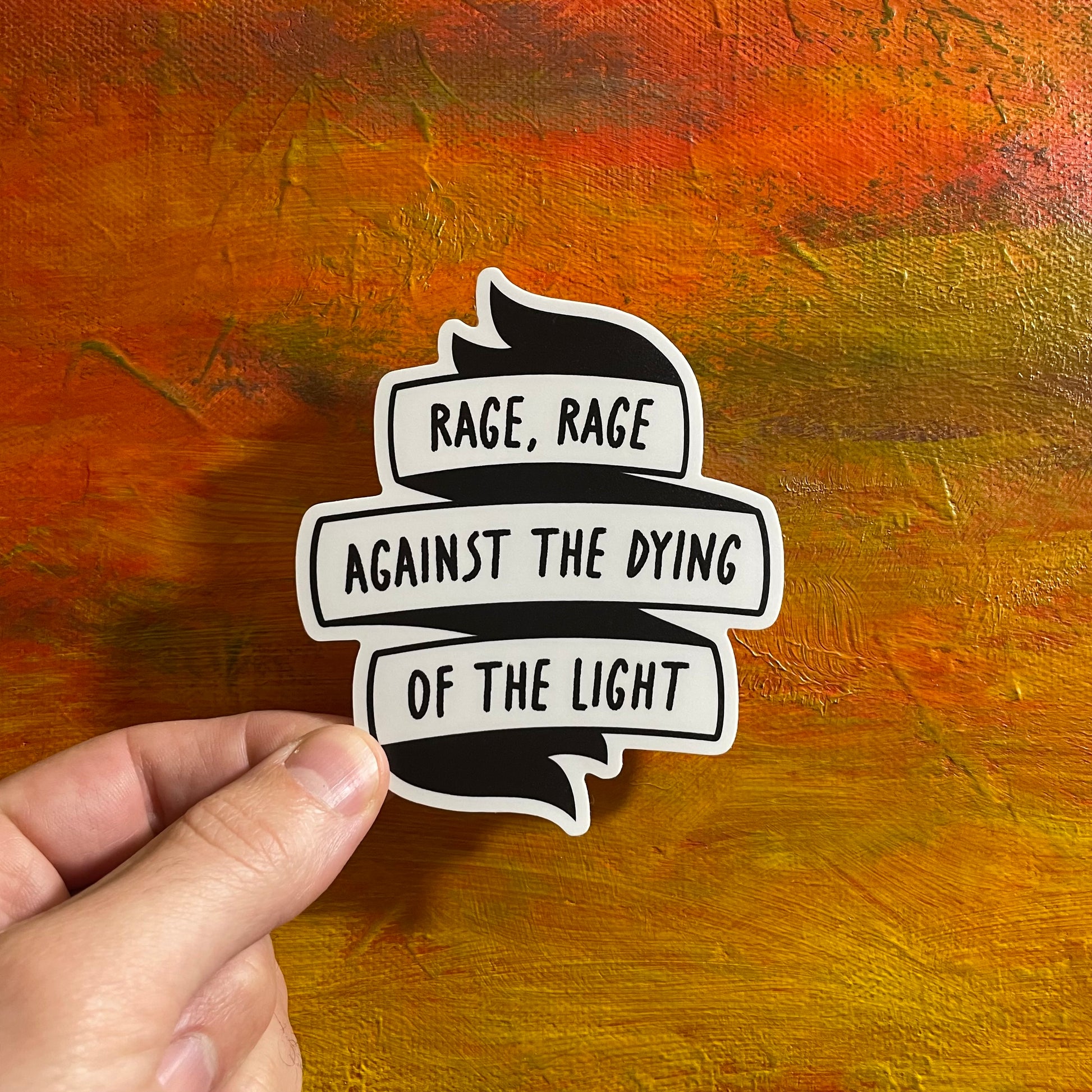 A black and white die cut sticker of a group of banners saying “rage, rage against the dying of the light”.